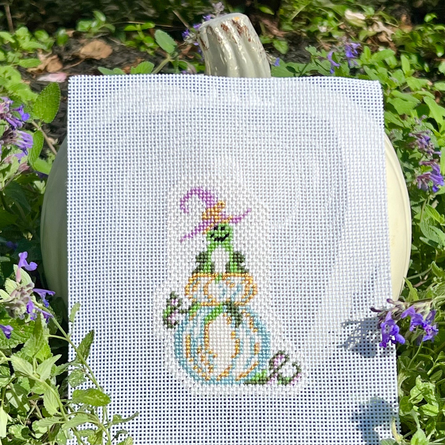 Needlepoint canvas design frog wearing witch hat on top of white pumpkin with gold and blue accents and trailing vines 